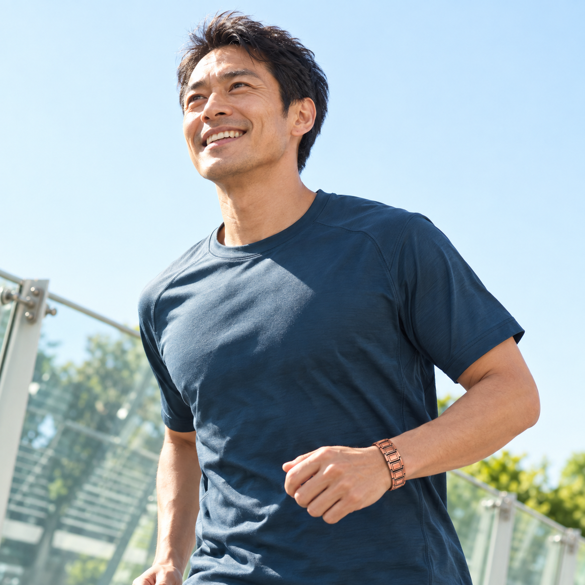 銅色のブレスレットを身につけ、青空の下で軽く走る男性。着用イメージ。